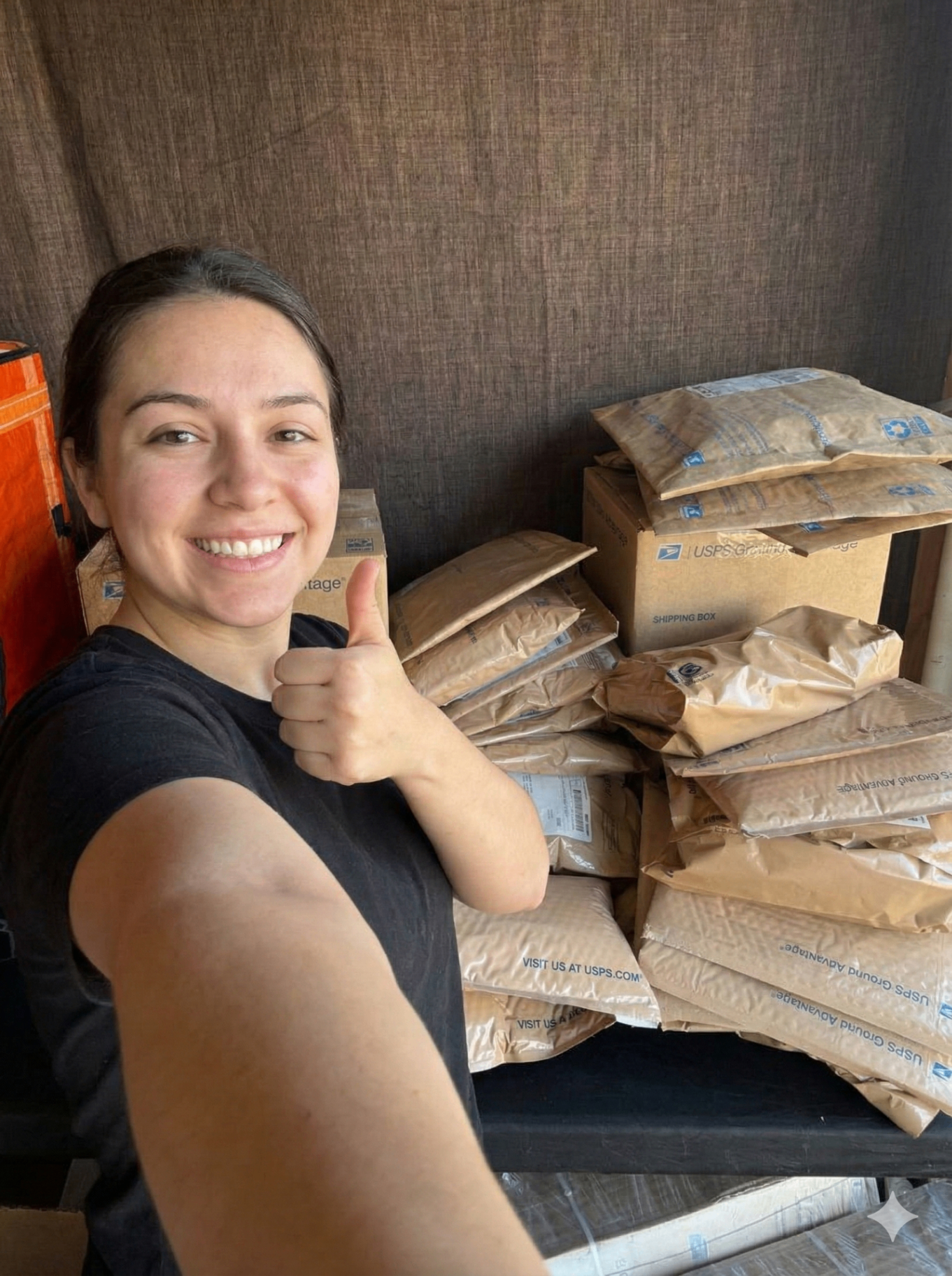 A smiling woman giving a thumbs up while taking a selfie in front of a large stack of packages and shipping boxes, showcasing successful business orders.